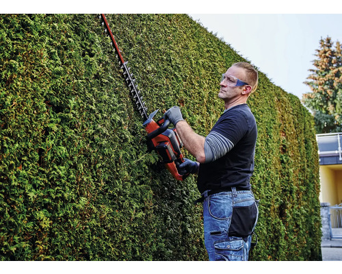 Muž strihá živý plot pomocou nožníc na živý plot a má pritom ochranné okuliare.