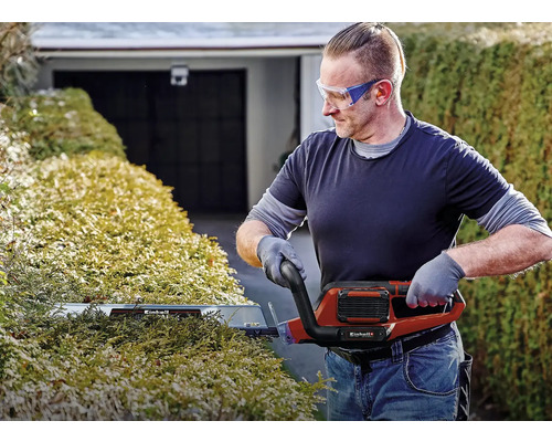 Muž strihá živý plot elektrickými nožnicami na živý plot od spoločnosti Einhell.