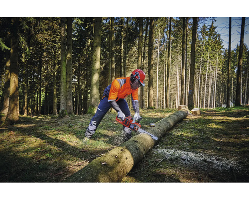 Osoba v ochrannom odeve reže motorovou pílou kmeň stromu v lese.