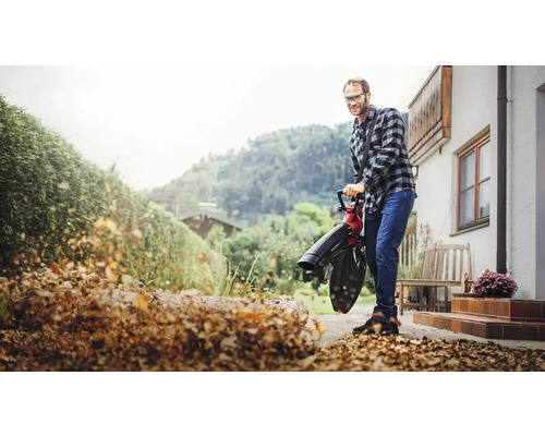 Muž používa vysávač lístia na prácu v záhrade pred domom.