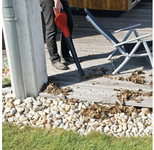 Osoba používa fúkač lístia na drevenej terase vedľa ležadla.
