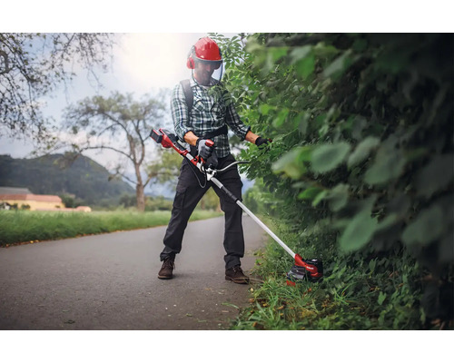 Osoba strihá živý plot pomocou akumulátorového vyžínača a ochranného odevu