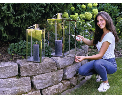 Žena zapaľuje sviečku vo svietniku v záhrade