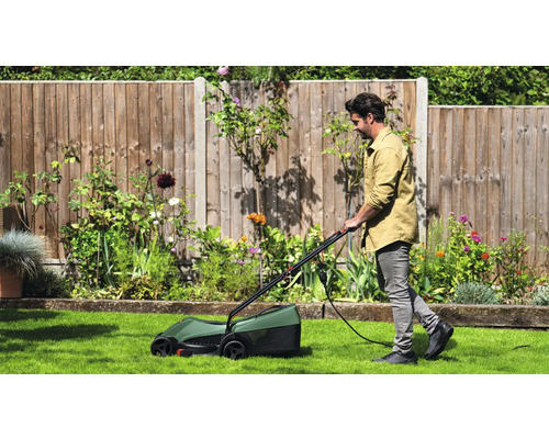 Muž kosí trávnik elektrickou kosačkou v záhrade.