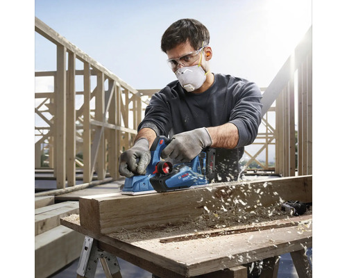 Remeselník používa elektrický hoblík Bosch na hobľovanie kusu dreva.