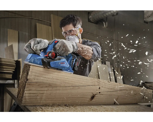 Muž hobľuje drevenú dosku elektrickým hoblíkom značky Bosch