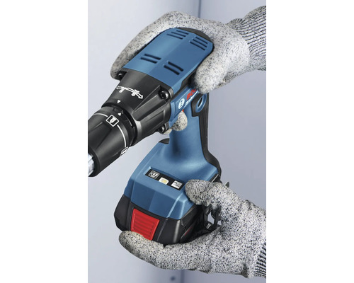 Osoba v rukaviciach drží akumulátorový skrutkovač na sadrokartón.