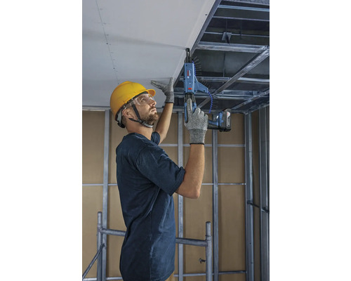 Remeselník upevňuje stropné dosky pomocou skrutkovača s podávačom