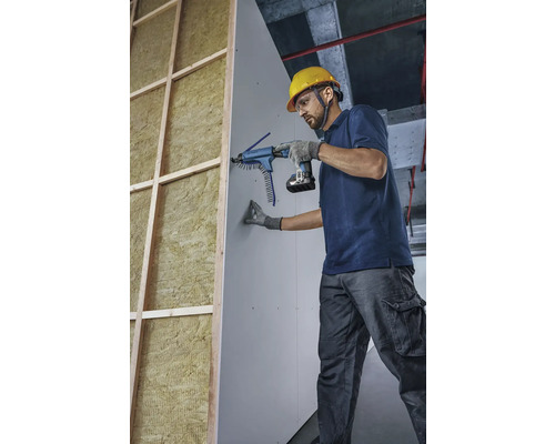 Remeselník pripevňuje sadrokartónovú dosku pomocou skrutkovača so zásobníkom k stene