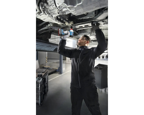 Mechanik pracuje s akumulátorovým rázovým uťahovákom na aute na zdviháku.