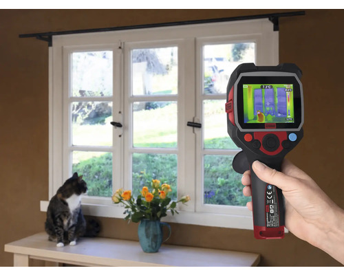 Ruka drží termokameru pred oknom, zatiaľ čo mačka sedí na parapete.