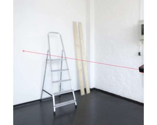 Pohľad do miestnosti s laserovým diaľkomerom na meranie vzdialeností, v pozadí rebrík a dve drevené dosky