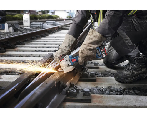 Pracovník reže uhlovou brúskou železničnú trať, pričom vznikajú iskry.