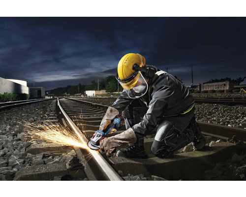 Pracovník brúsi železničnú koľajnicu uhlovou brúskou a iskrí.