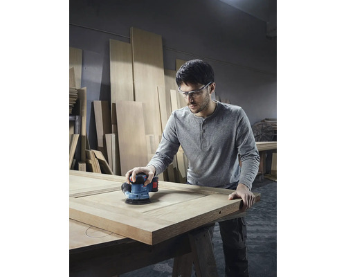 Muž brúsi drevené dvere excentrickou brúskou v dielni