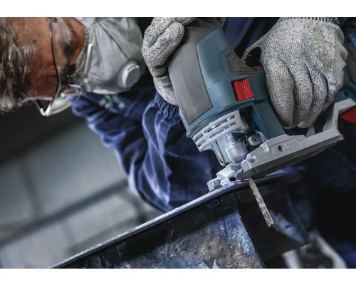 Muž reže kov priamočiarou pílou. Má na sebe ochranné okuliare, masku na tvár a rukavice.