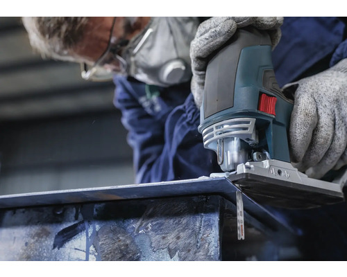 Osoba s respirátorom reže kus kovu priamočiarou pílou.