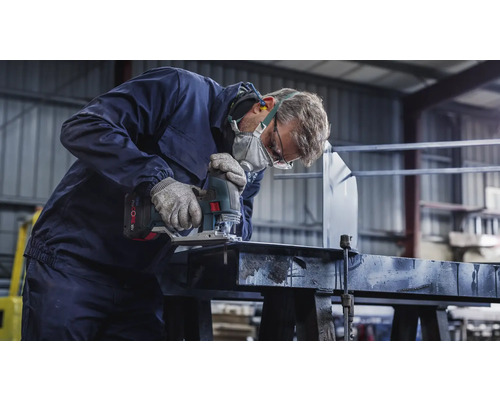 Remeselník s ochrannou maskou a okuliarmi reže obrobok priamočiarou pílou.