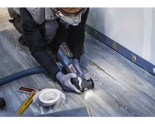 Remeselník používa multifunkčný nástroj na laminátovej podlahe na renováciu.