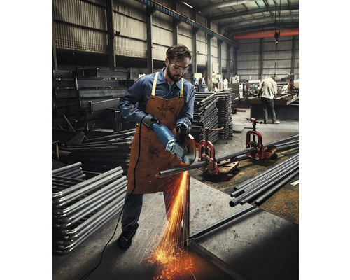 Muž v dielni reže uhlovou brúskou kovovú rúrku, od ktorej odletujú iskry.