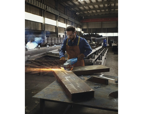 Muž brúsi kov uhlovou brúskou v dielni.