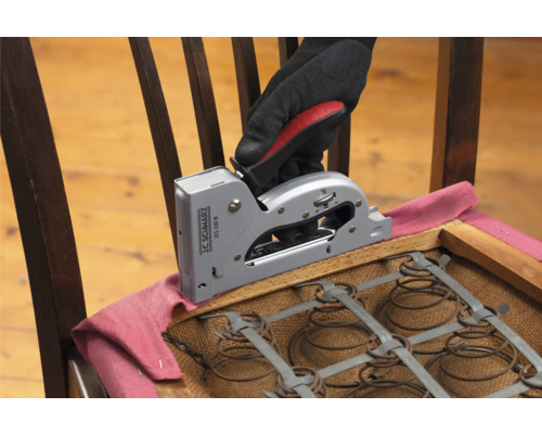 Ruka v rukavici pripevňuje látku ručnou sponkovačkou na stoličku.