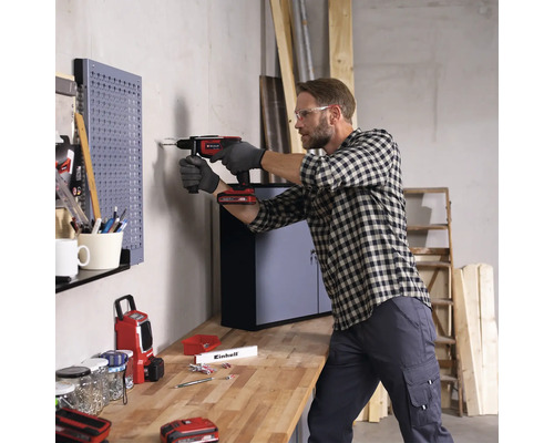 Muž vŕta akumulátorovým skrutkovačom do steny v dielni