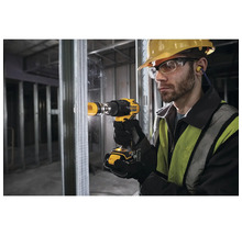 Muž vŕta vŕtačkou otvor do kovovej steny. Má ochranné okuliare, prilbu a štuple do uší.