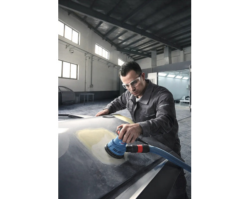 Muž brúsi kapotu auta excentrickou brúskou v dielni.