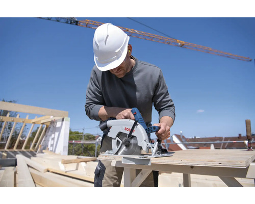 Remeselník s ochrannou helmou reže drevo okružnou pílou Bosch na stavenisku.