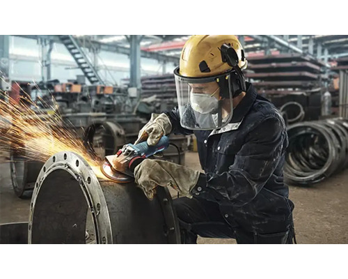 Robotník brúsi kovovú rúrku flexou, z ktorej odlietajú iskry.