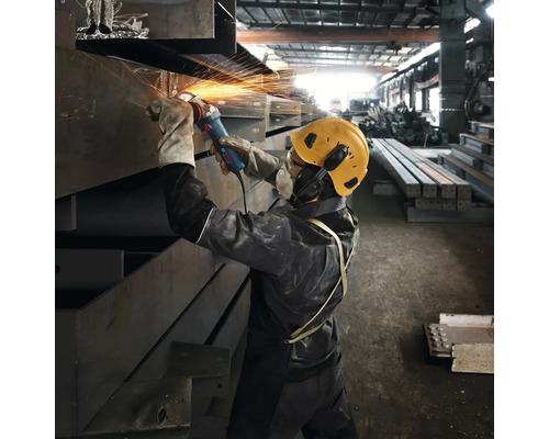 Robotník brúsi kov uhlovou brúskou v továrnej hale, zatiaľ čo lietajú iskry.