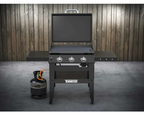 Plynový grilovací vozík Tenneker s plynovou fľašou pred drevenou stenou