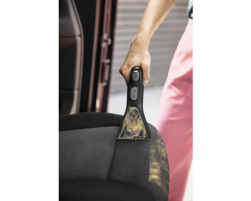 Detailný záber osoby čistiacej autosedačku pomocou prenosného čističa škvŕn.