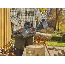 Osoba drží akumulátorovú reťazovú pílu Gardena nad pňom v záhrade.