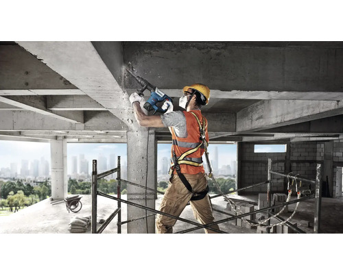 Stavebný robotník s búracím kladivom vykonáva betonárske práce na stavenisku.