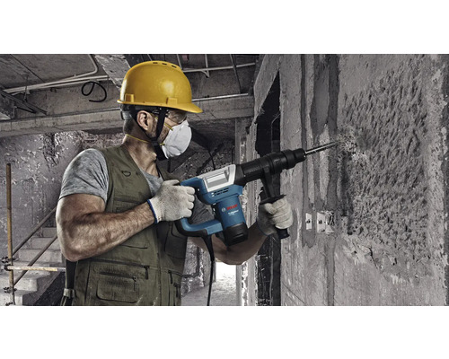 Remeselník vŕta dieru do betónovej steny pomocou vŕtacieho kladiva.
