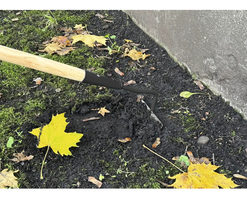 Detailný záber motyky s drevenou rukoväťou v záhradnej pôde.