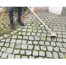 Osoba čistí kamennú dlažbu kefou na škáry