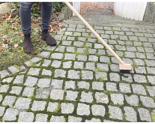 Osoba čistí kamennú dlažbu kefou na škáry