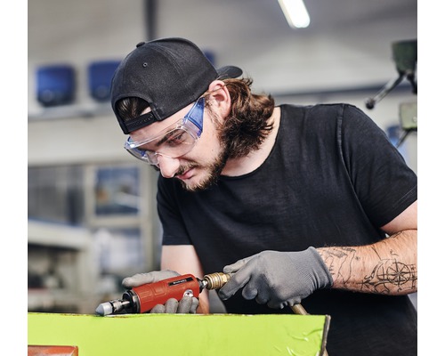 Muž s ochrannými okuliarmi a rukavicami používa pneumatickú brúsku.