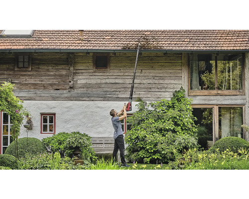 Muž čistí odkvap pomocou čističa odkvapov pred domom.