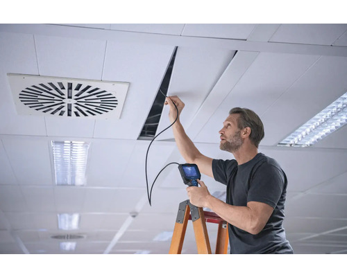 Muž s endoskopom vykonáva inšpekciu stropu na rebríku