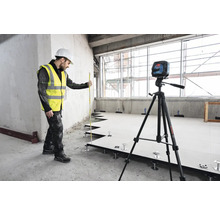 Remeselník s laserovou vodováhou a nivelačnou latou pri inštalácii zdvojenej podlahy.