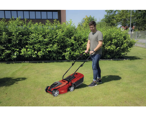 Muž kosí trávnik kosačkou na trávu v záhrade.