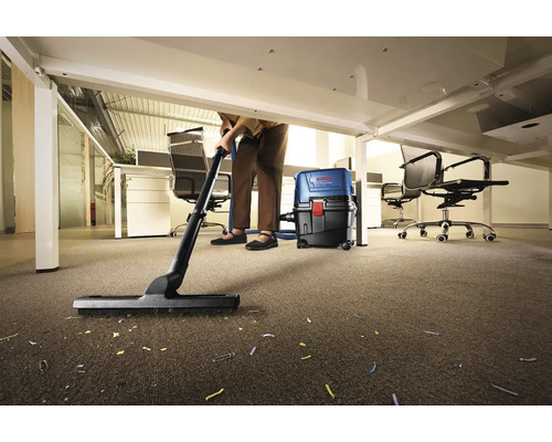 Osoba upratuje vysávačom koberec v kancelárii pod stolom.