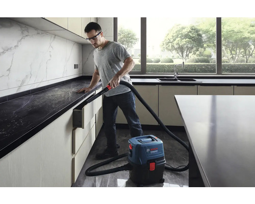 Muž používa mokrý suchý vysávač Bosch Professional v modernej kuchyni na odstránenie prachu.