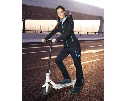 Žena so softshellovou bundou, pracovnými nohavicami a bezpečnostnou obuvou na elektrickej kolobežke