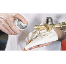 Osoba čistí regulátor tlaku plynu sprejom a handričkou.