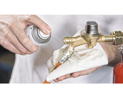 Osoba čistí regulátor tlaku plynu sprejom a handričkou.